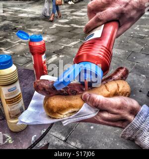 Mann, der Tomatensauce auf Deutsch, Bratwurst Wurst in einer Rolle Stockfoto