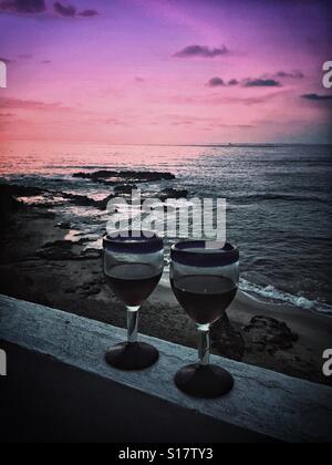 Zwei Gläser Rotwein im mexikanischen mundgeblasenen Weingläsern serviert auf einem Balkon mit Blick auf die zerklüftete Küste von Nayarit bei Sonnenuntergang. Stockfoto