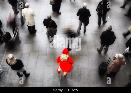Blick von oben auf einen belebten Bahnhofshalle mit einer einsamen Frau in rot stehen, aus einer Menge von Bahn-Pendler und Passagiere. Stockfoto