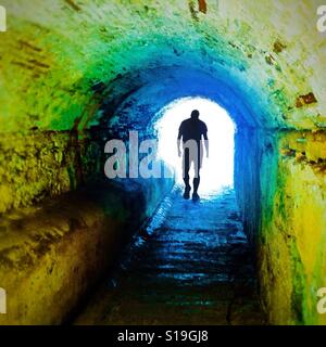 Anonyme Silhouette einer Person zu Fuß durch eine dunkle Unterführung symbolisiert Licht am Ende des Tunnels Stockfoto