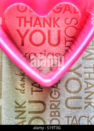 Rosa Kunststoff Herzform über einem Hintergrund das Wort danke in verschiedenen Sprachen Stockfoto