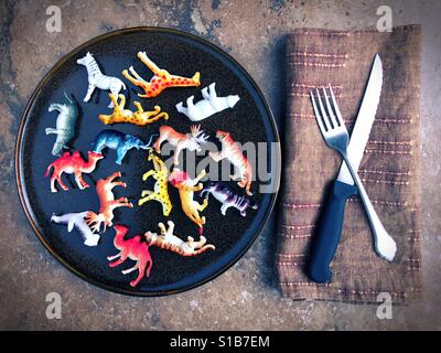 Kunststoff-Spielzeugtiere auf einem Teller neben Messer und Gabel. Stockfoto