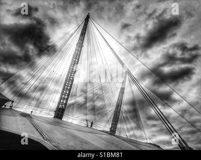 Schwarz / weiß Foto von der Sonne hinter dramatische Wolken über die O2-Arena in North Greenwich, Lindon, England, UK. Stockfoto