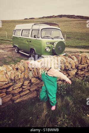 Junges Mädchen im grünen Hosen neben einer Trockensteinmauer mit einem Erker grün Typ 2 Vw Campingbus Stockfoto