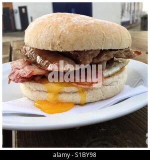 Ein leckeres Frühstück Bap/Roll aus einem Straßencafé gefüllt mit Speck, Wurst und Ei. Reich an Cholesterin und Fett ist das kein gesundes Frühstück Stockfoto