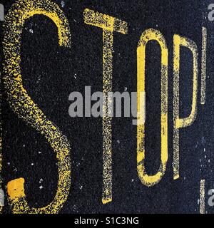 Gelb lackierte Straße Kennzeichnung Zeichen auf schwarzem Asphalt mit dem Wort Stop. Stockfoto