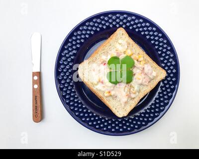 Schnittbrot garniert mit Thunfisch, verteilt auf eine blaue Platte und ein Buttermesser Stockfoto