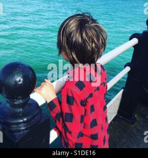 Kleiner Junge im roten Hemd mit Blick auf Meer Stockfoto