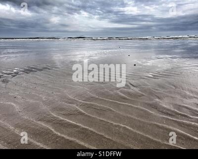 Grate in Sand und Schein des Lichts in den Untiefen des Meeres in Cymyran Strand, Rhosneigr, Anglesey, North Wales, Stockfoto