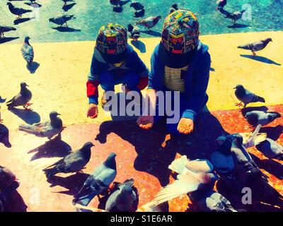 Zwei junge Brüder hocken und Knien auf Futtermittel Tauben. Stockfoto