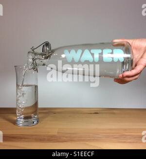 Frisches Trinkwasser fließt aus einer Hand statt Flasche mit einem print 'Wasser' in ein Trinkglas Stockfoto