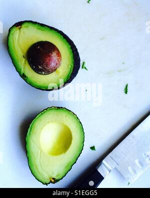 Avocado in Scheiben geschnitten in der Hälfte mit Messer auf Schneidebrett Stockfoto