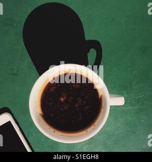 Eine obenliegende Aufnahme eines frischen Kaffee Americano Getränks am grünen Tisch mit einem Smartphone. Stockfoto