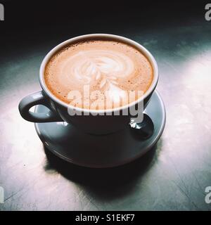 Ein overhead Nahaufnahme von einem frischen Latte Kaffee-Getränk auf Metall Tischplatte. Eine einfache, saubere Komposition. Stockfoto