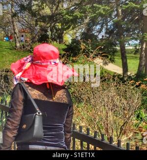 Dame mit einem roten Hut mit breiter Krempe im Park spazieren. Stockfoto