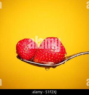 Frische Erdbeeren in einem Löffel vor einem gelben Hintergrund Stockfoto