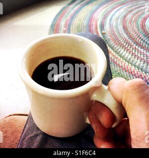 Nahaufnahme von einer Tasse Kaffee auf einen Mann Bein ruht Stockfoto