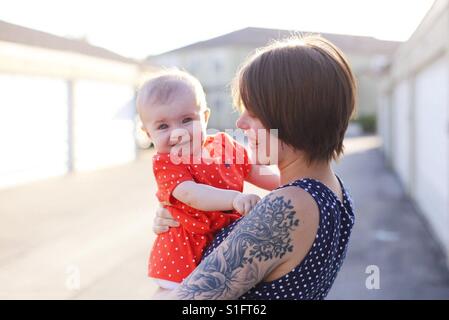 Hippe junge Mutter mit Tattoos und kurze Haare Baby Tochter glücklich hielt Stockfoto