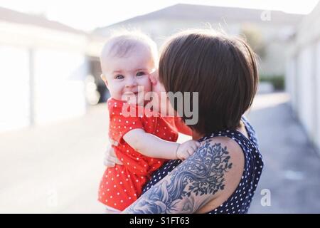 Hippe junge Mutter mit kurzen Haaren und Tattoos halten Baby Mädchen Tochter auf Wange küssen Stockfoto