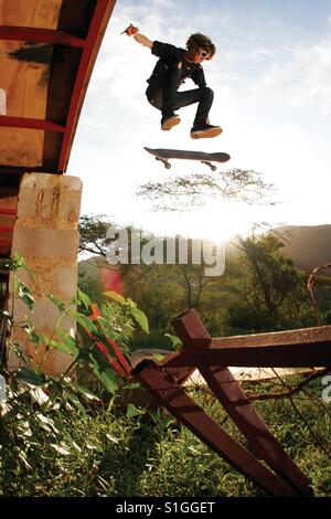 Ein Junge Skateboarder führt einen radikalen Schritt, wie er durch die Luft fliegt. Stockfoto