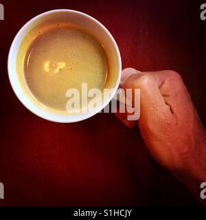 Eines Mannes Hand hält ein frisches Americano Getränk ruht auf einem rotem Ledersitz Stockfoto