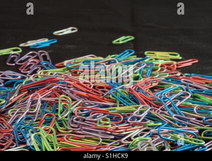 Ein Haufen von Büroklammern in vielen verschiedenen Farben vor einem schwarzen Hintergrund. Stockfoto