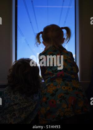 Silhouette von zwei Kindern Blick Zugfenster, von hinten mit blauem Himmelshintergrund. Stockfoto