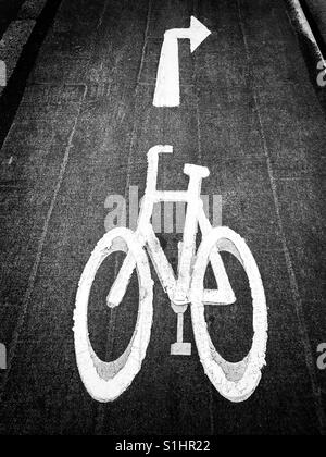 Eine gemalte weiße Symbol eines Fahrrades in einem städtischen Gebiet - Dies ist eine spezielle Radweg. Der Pfeil zeigt, dass Radfahrer vorne rechts oben abbiegen müssen. Bildnachweis - © COLIN HOSKINS. Stockfoto