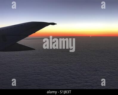 Die Sonne lugt hinter dem Horizont als Morgenrot über dem Flügel eines Flugzeuges im Flug. Stockfoto
