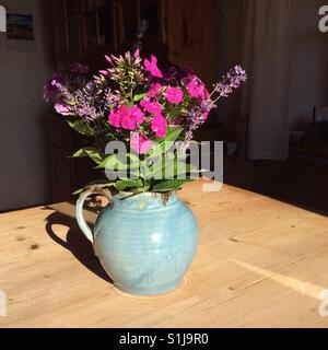 Bouquet von blühenden Blumen, wie Phlox und Lavendel aus dem Garten in einem blauen Ton Glas auf einem Holztisch im Garten in einem Bauernhaus Stockfoto