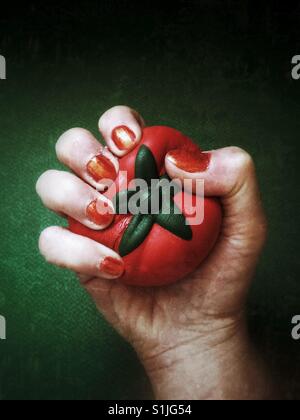 Die Hand einer Frau drückte eine Tomate geformt Stress-ball Stockfoto