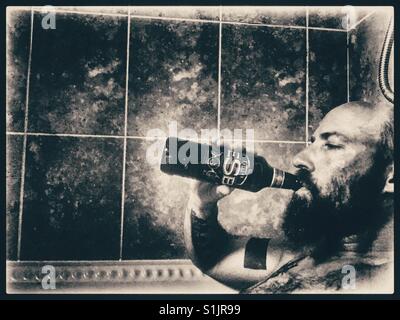 Bärtige tätowierter Mann echtes Ale zu trinken aus der Flasche in ein heißes Bad. Stockfoto