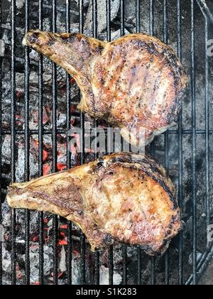 2 Schweinekoteletts Grillen auf einem Holzkohlegrill. Stockfoto