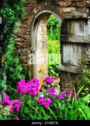 Blick auf einen englischen Garten Torbogen mit Tür aus Holz. Es ist Sommer, so dass die Blumen bunt sind und in voller Blüte. Bildnachweis - © COLIN HOSKINS. Stockfoto