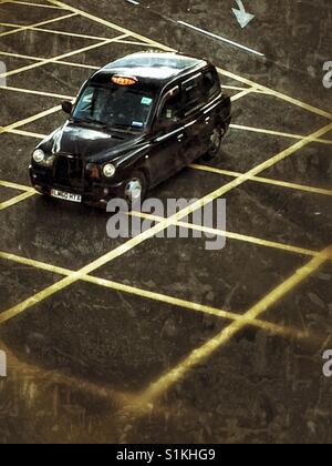 Blick von oben auf einen schwarzen Londoner Taxis oder Taxi Beschleunigung über gelbe Gefahr Linien auf einer Londoner Straße. Stockfoto