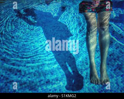 Frau, Schwimmen im Pool mit eine Pool-Nudel und ihren Schatten auf den gefliesten Boden des Beckens. Stockfoto