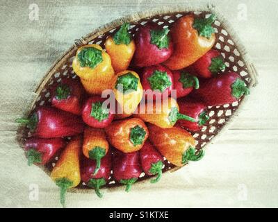 Homegrown Bio rot, gelb und Orange gefärbt Paprika in einem Korb auf einem Holztisch. Stockfoto