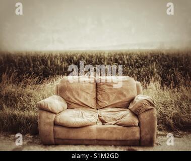 Abgebrochene Couch auf der Seite der Landstraße mit Kornfeld im Hintergrund. Delta, British Columbia, Kanada. Stockfoto