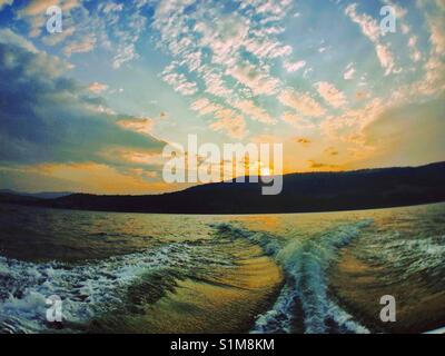 Ein Blick zurück auf Sonnenuntergang über einem Berg vom Boot aus. Stockfoto