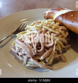 Hausgemachten Salat aus Streifen von Wurst, Käse auf weiße Platte und Bayerische Brezel. Schweizer Wurstsalat. Stockfoto