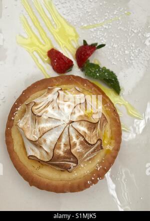 Auf leckere Lemon Meringue Tarte mit Erdbeere und Minze garnieren auf weiße Platte mit Puderzucker bestäubt Stockfoto