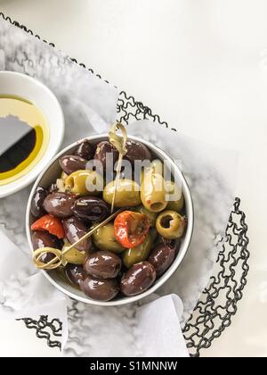 Kleine weiße Teller saftig grünen und schwarzen Oliven und getrocknete Tomaten in Drahtkorb mit Olivenöl und Balsamico auf der Seite eingestellt. Stockfoto