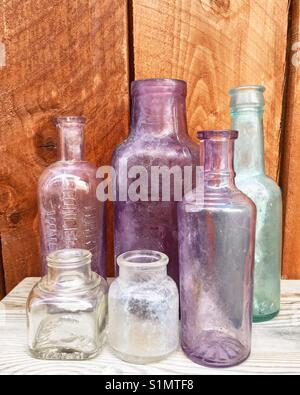 Eine Sammlung von klassischen und antiken geblasenem Glas und Maschine an Flaschen auf Holz Tisch mit Holz Zaun Hintergrund. Enthält Tinte, Medizin, und würze Flaschen. Stockfoto