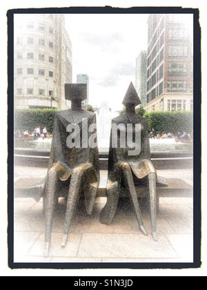 Paar Statuen sitzt auf der Bank am Canary Wharf in London. Stockfoto