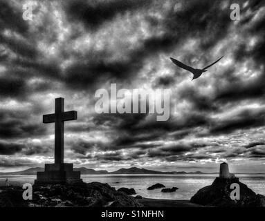 Kreuz Memorial und Leuchtturm auf llanddwyn Island aus Whitby Strand auf Anglesey, Nordwales. Stockfoto