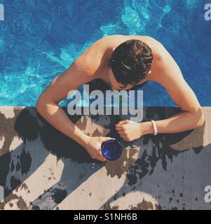 Junger Mann in einem Schwimmbad, beugte sich über den Pool Deck, während Sie ein Getränk an einem sonnigen Tag. Platz crop. Stockfoto