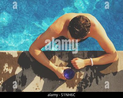 Junge Mann in Schwimmbad beugte sich über die Kante, während Sie ein Getränk in der Hand auf einem sonnigen, heissen Tag. Stockfoto