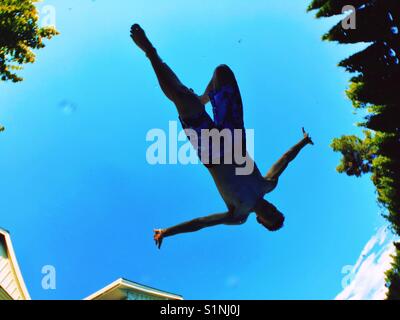 Teenager fotografiert von unten, wie er durch die Luft fliegt weg von einem Sprungbrett ins Schwimmbad ist. Stockfoto