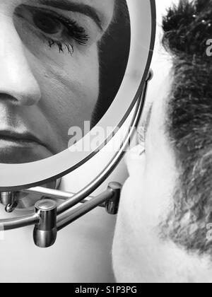 Eine schwarz-weiße Nahaufnahme einer Frau, die ihre Spiegelung in einem Schminkspiegel vergrößert betrachtet Stockfoto