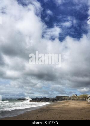 Einsames Haus am Strand mit Wellen gegen Felsen, Rhosneigr, Anglesey, Nordwales Stockfoto